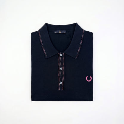 A folded dark navy polo shirt with pink contrast stitching and a pink embroidered laurel wreath logo on the left chest, displayed on a clean white background.