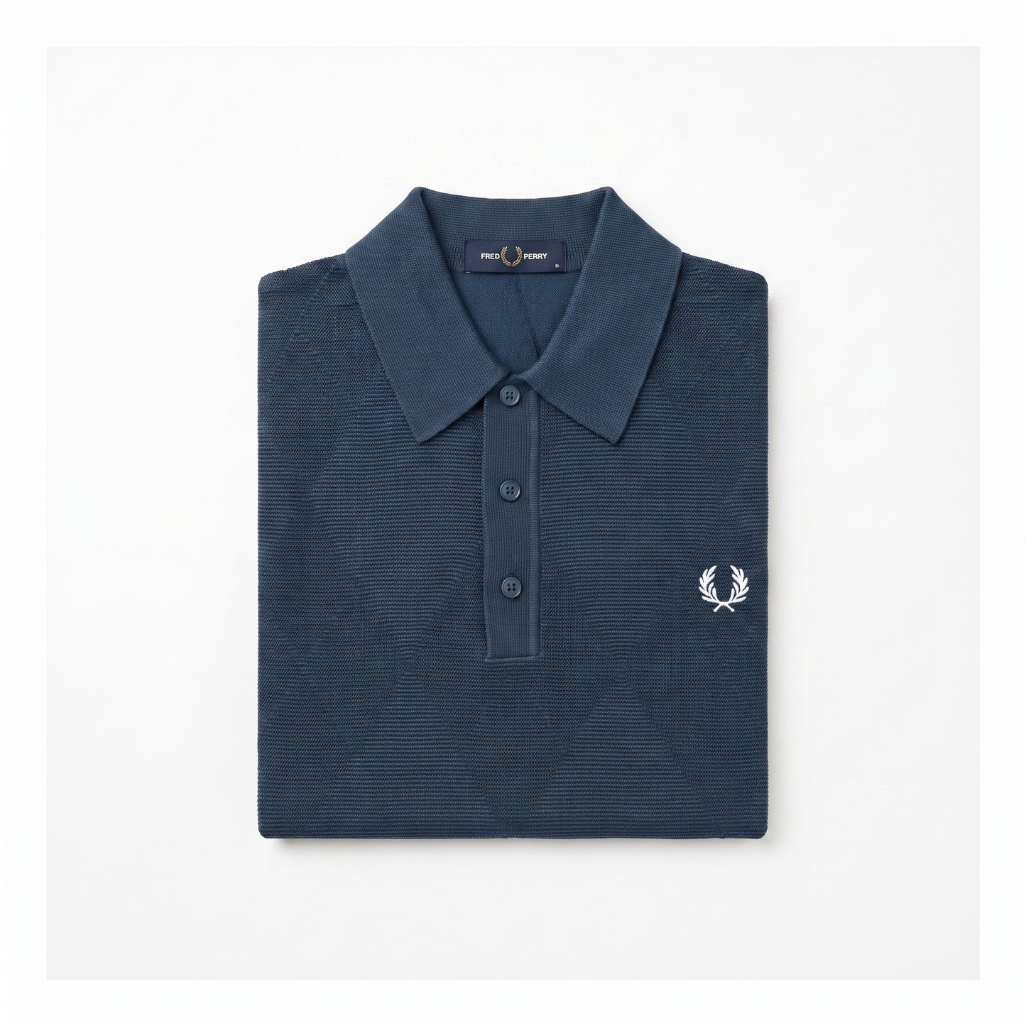 A folded navy blue polo shirt with a textured waffle knit pattern, featuring a white embroidered laurel wreath logo on the left chest, set against a plain white background.