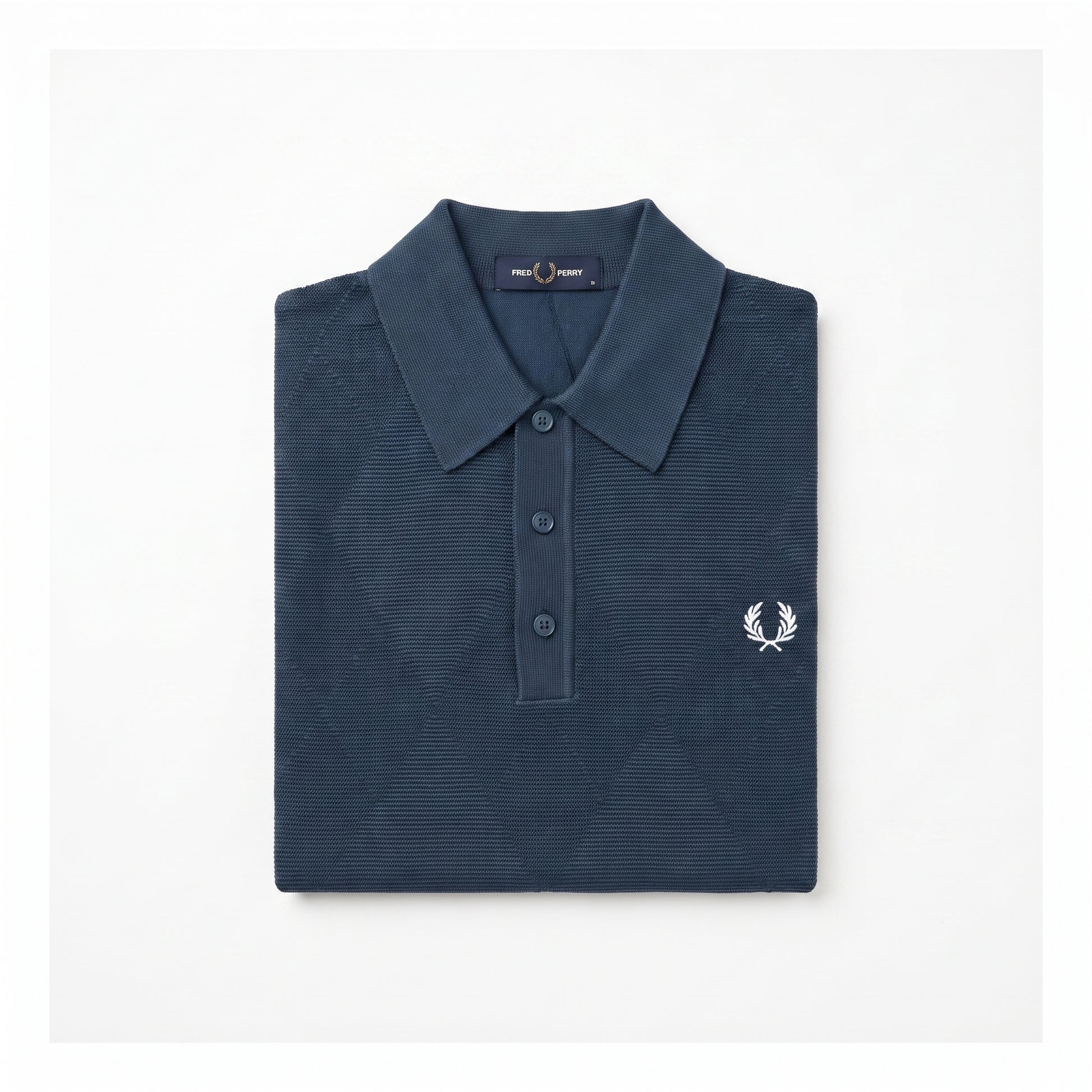 A folded navy blue polo shirt with a textured waffle knit pattern, featuring a white embroidered laurel wreath logo on the left chest, set against a plain white background.