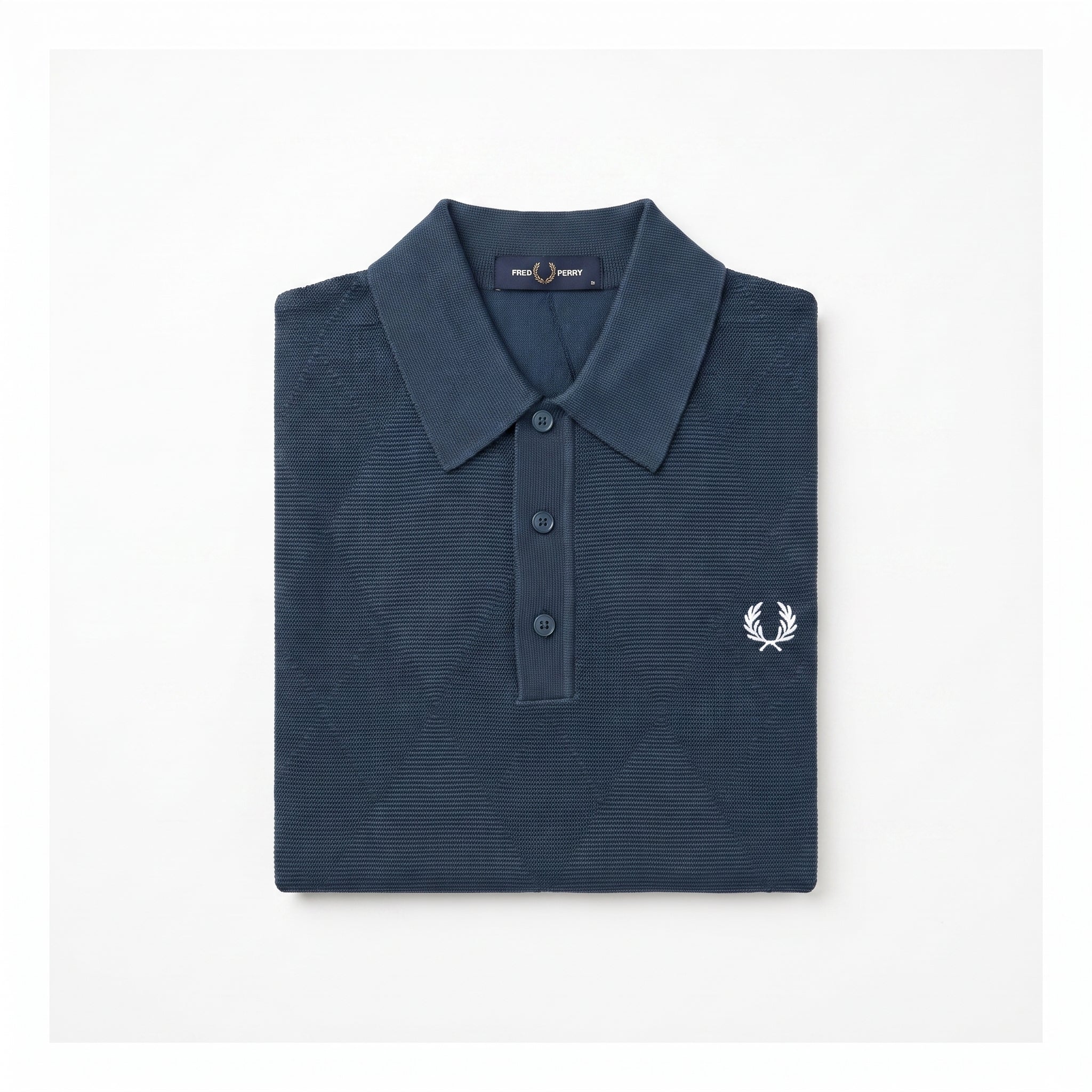 A folded navy blue polo shirt with a textured waffle knit pattern, featuring a white embroidered laurel wreath logo on the left chest, set against a plain white background.