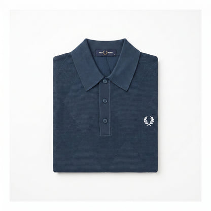 A folded navy blue polo shirt with a textured waffle knit pattern, featuring a white embroidered laurel wreath logo on the left chest, set against a plain white background.
