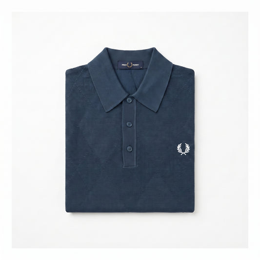 A folded navy blue polo shirt with a textured waffle knit pattern, featuring a white embroidered laurel wreath logo on the left chest, set against a plain white background.
