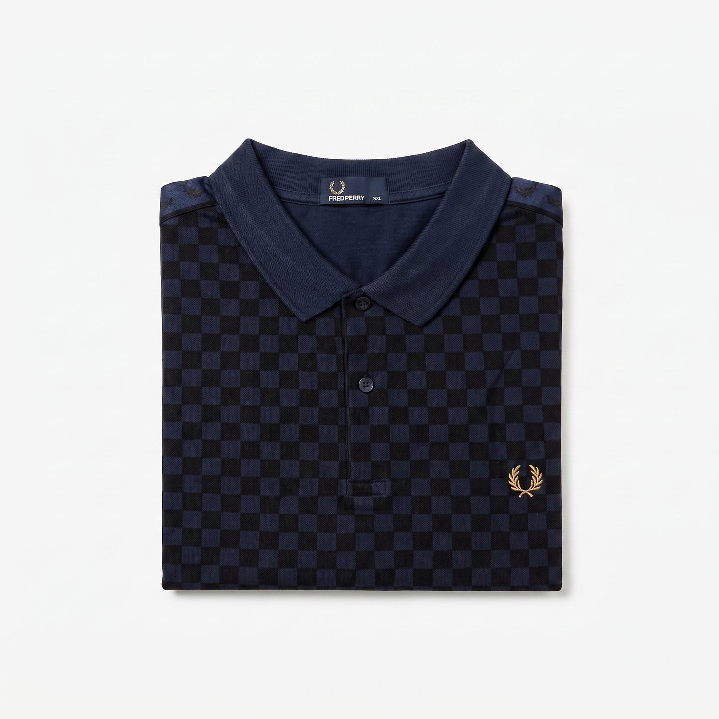 A folded navy blue polo shirt with a dark blue and black checkerboard pattern, featuring a small gold embroidered laurel wreath logo on the left chest. The brand label inside the collar reads ‘Fred Perry’