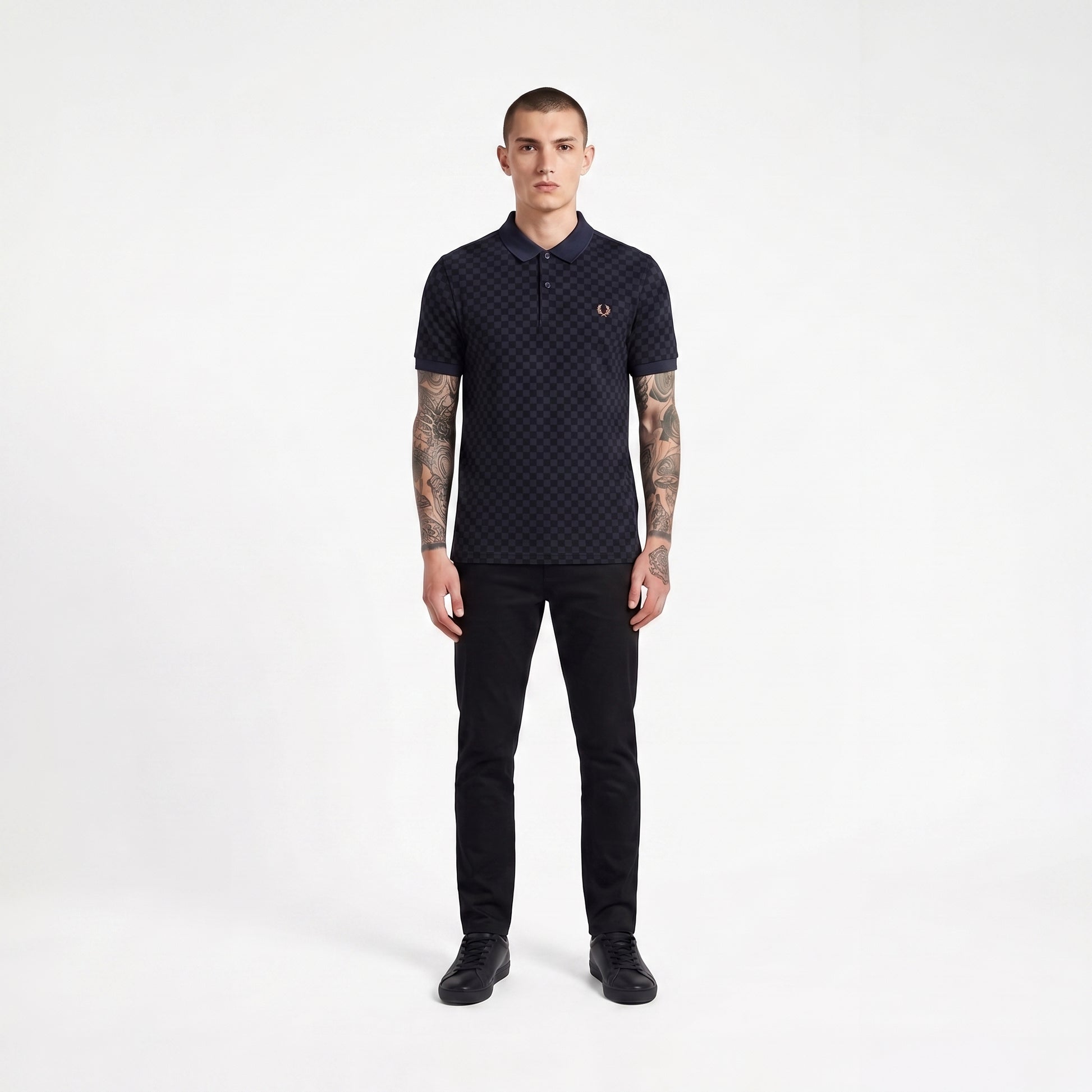 A man modeling a dark navy short-sleeve polo shirt with a subtle geometric pattern and a small embroidered laurel wreath logo on the chest, paired with black trousers and black shoes, against a plain white studio background.