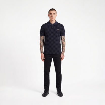 A man modeling a dark navy short-sleeve polo shirt with a subtle geometric pattern and a small embroidered laurel wreath logo on the chest, paired with black trousers and black shoes, against a plain white studio background.