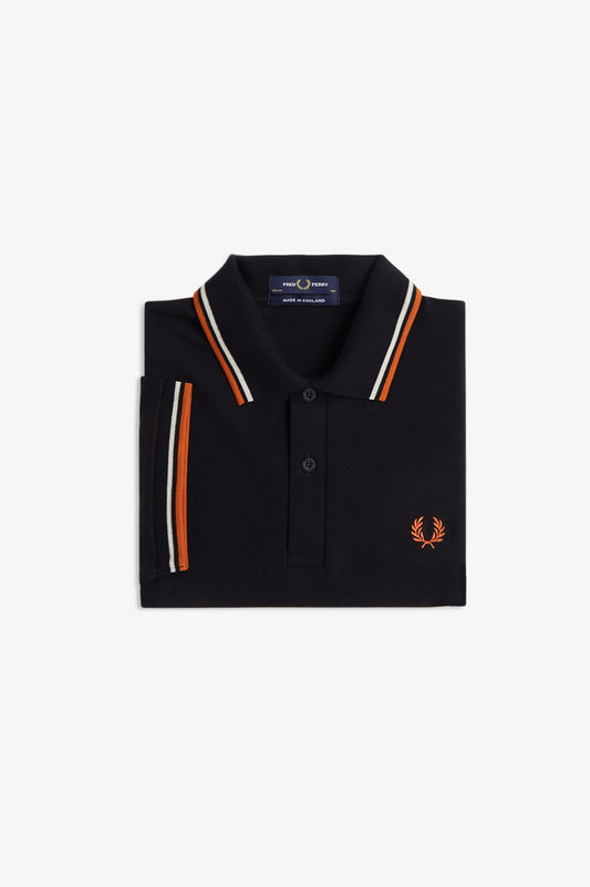 A folded black polo shirt with orange and white striped trim on the collar and sleeve cuffs, featuring the signature orange laurel logo on the left chest, set against a plain light gray background.