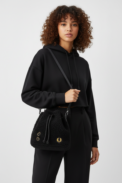 Woman wearing a black hoodie and pants holding a matching black drawstring bag on a white background