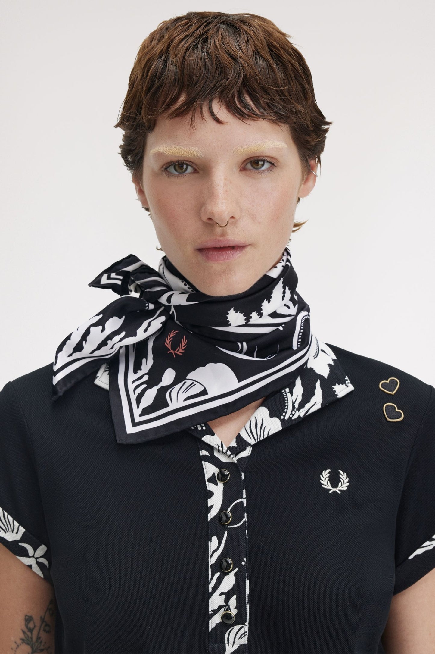 Person wearing a black and white patterned scarf with a visible brand logo on a plain background