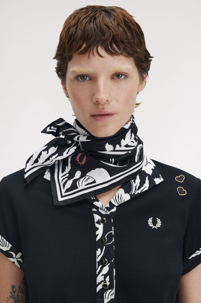 Person wearing a black and white patterned scarf with a visible brand logo on a plain background