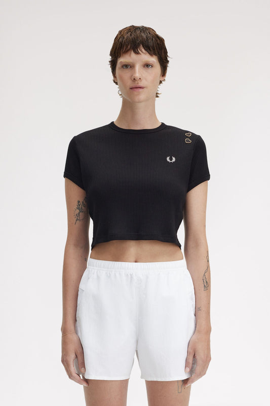 A woman wearing a black ribbed t-shirt with embroidered hearts and a Laurel Wreath logo, paired with white shorts.