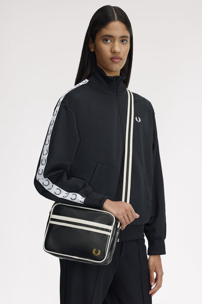 Person wearing a black outfit with white stripes holding a black bag featuring a brand logo.
