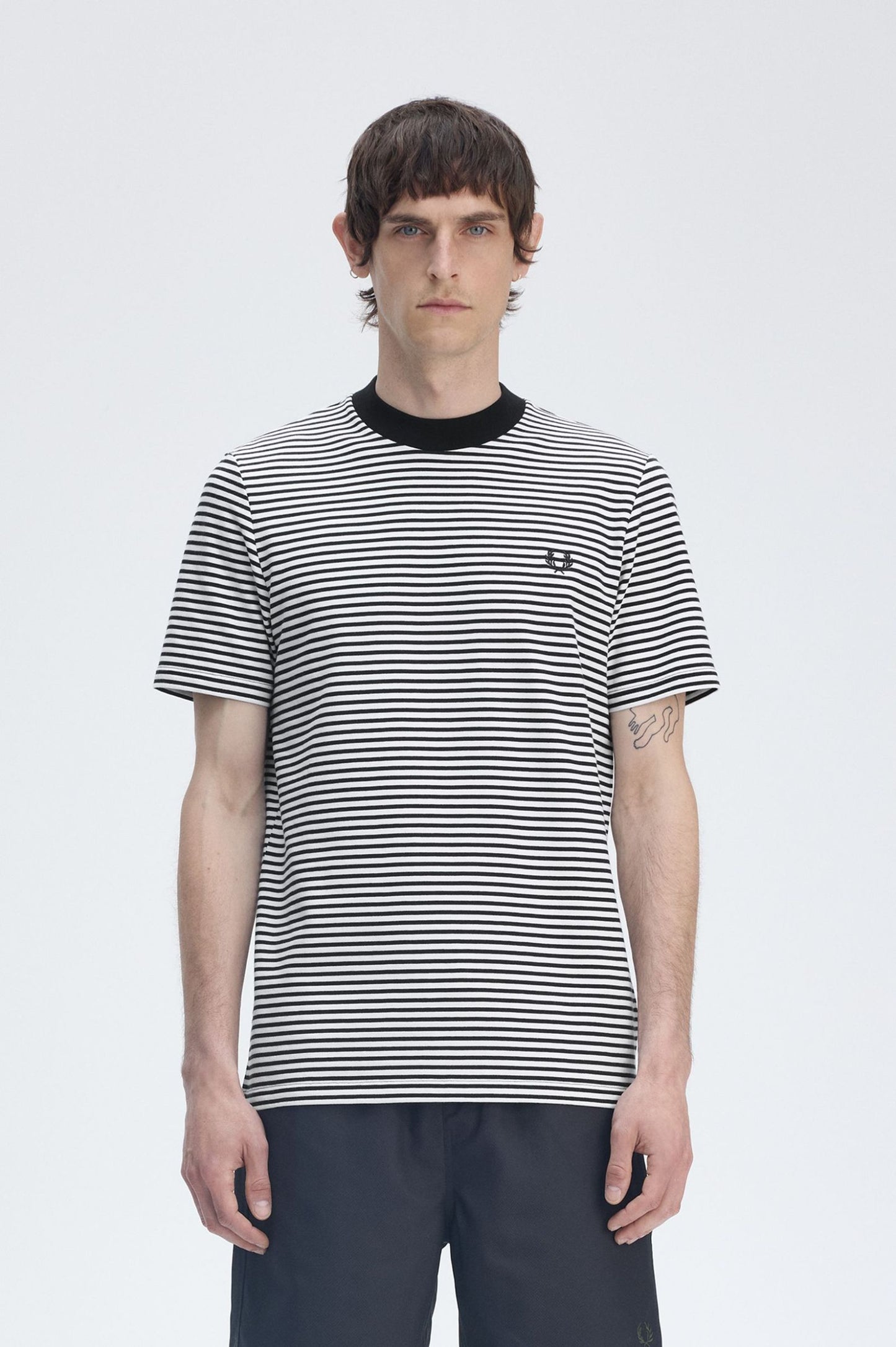 A man wearing a slim fit, black and white striped t-shirt with the Laurel Wreath logo on the left chest.