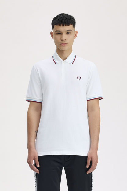 Person wearing a white polo shirt with red and blue accents on a plain background
