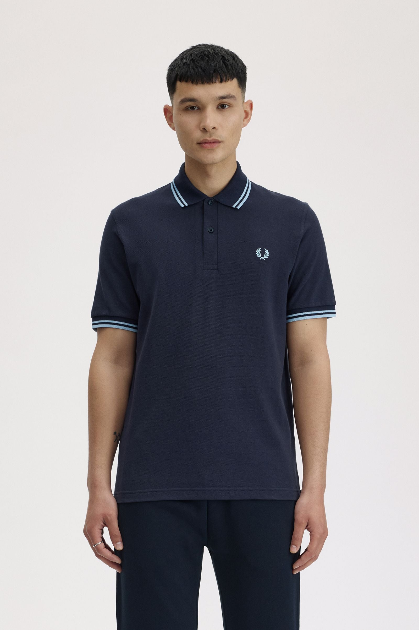 Person wearing a navy polo shirt with a brand logo on a light background