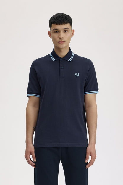 Person wearing a navy polo shirt with a brand logo on a light background