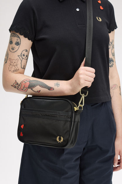 Person wearing a black polo shirt with a brand logo, holding a black bag with a brand logo.