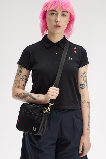 Person wearing a black polo shirt with embroidered details, holding a black bag against a white background