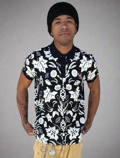 A person wearing a black and white botanical print polo shirt with a collar, solid cuffs, and a branded button closure.