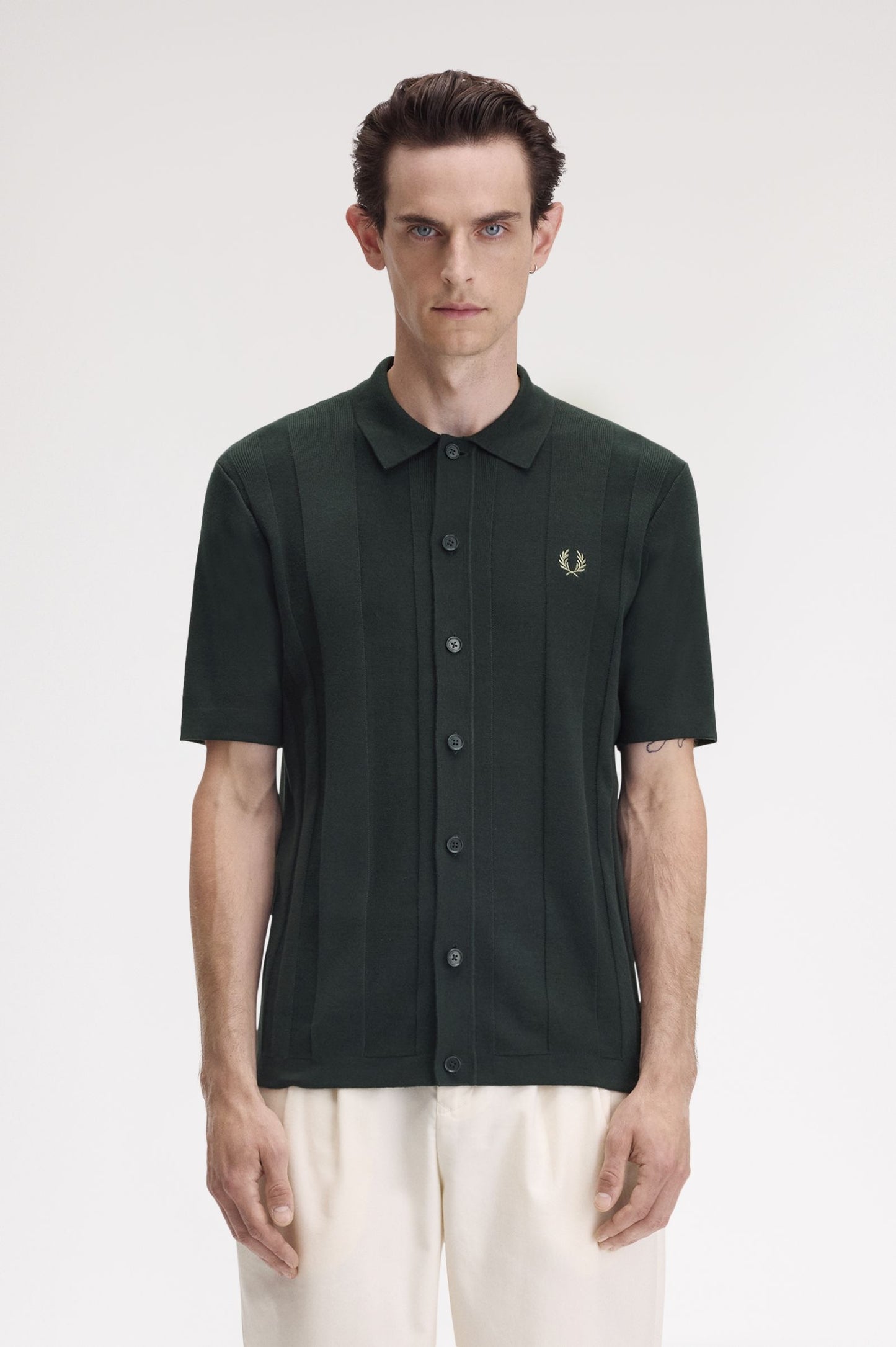 A male model wearing a night green Fred Perry button-through short-sleeve shirt.