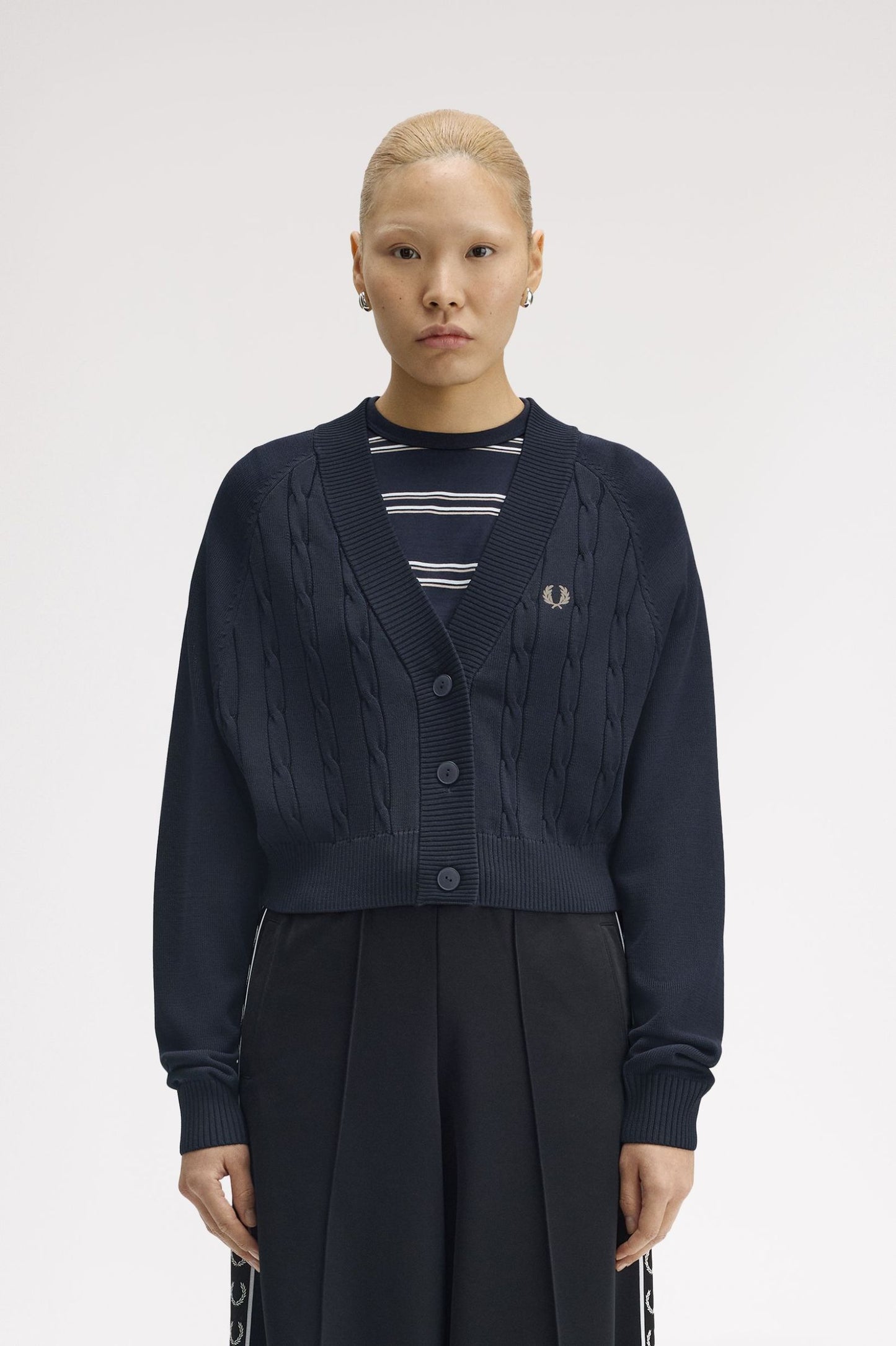 Person wearing a navy cardigan over a striped shirt with a visible brand logo on a white background