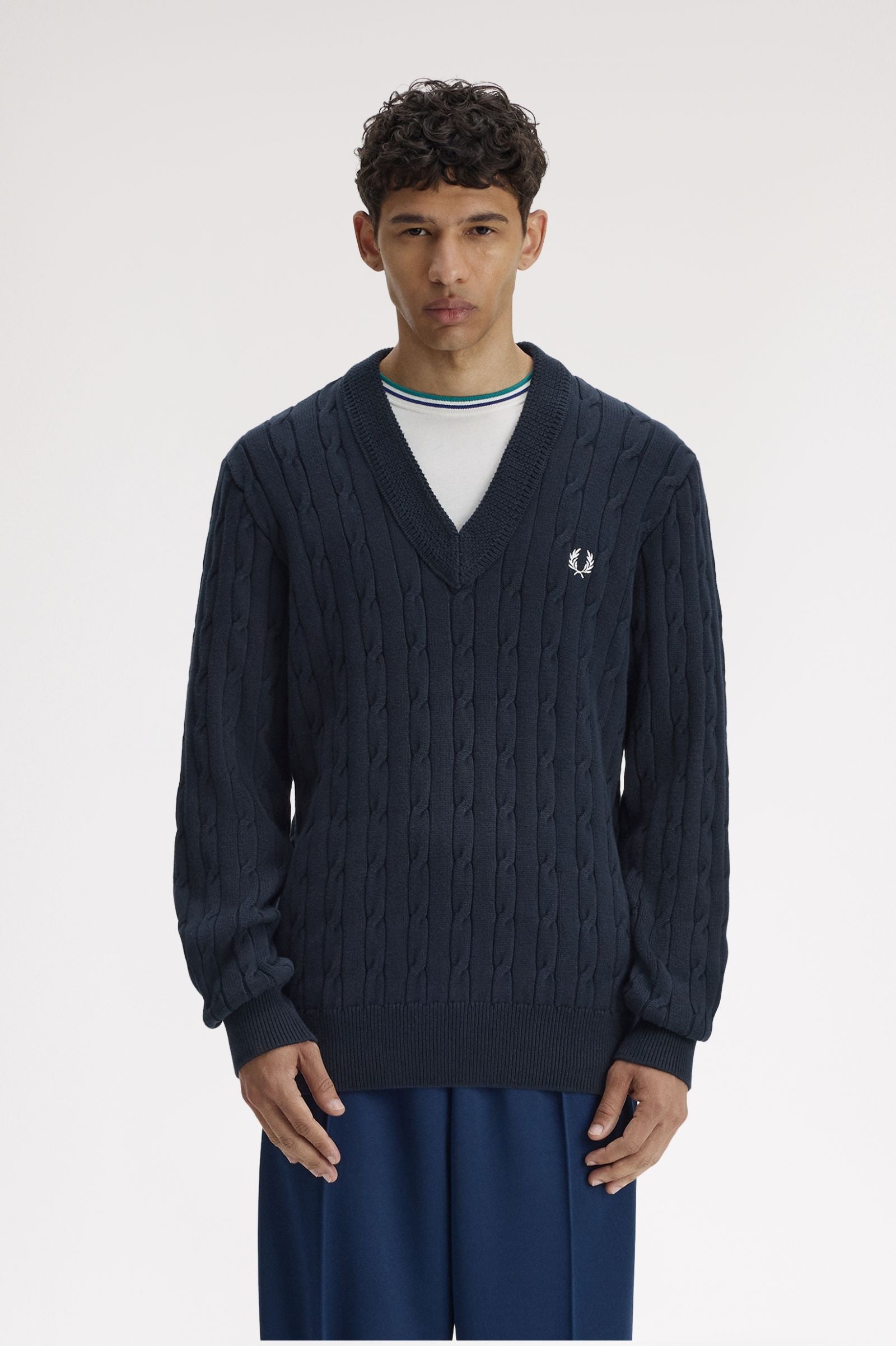 Man wearing a navy cable knit sweater with a brand logo on a white background