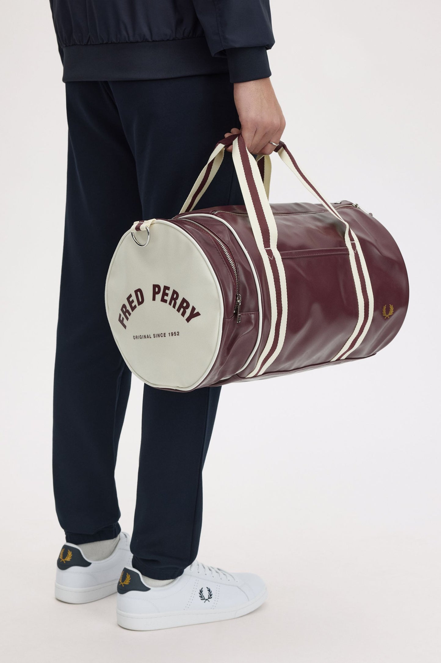 Person holding a maroon duffel bag with 'Fred Perry' branding on a white background