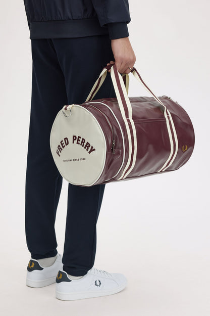 Person holding a maroon duffel bag with 'Fred Perry' branding on a white background