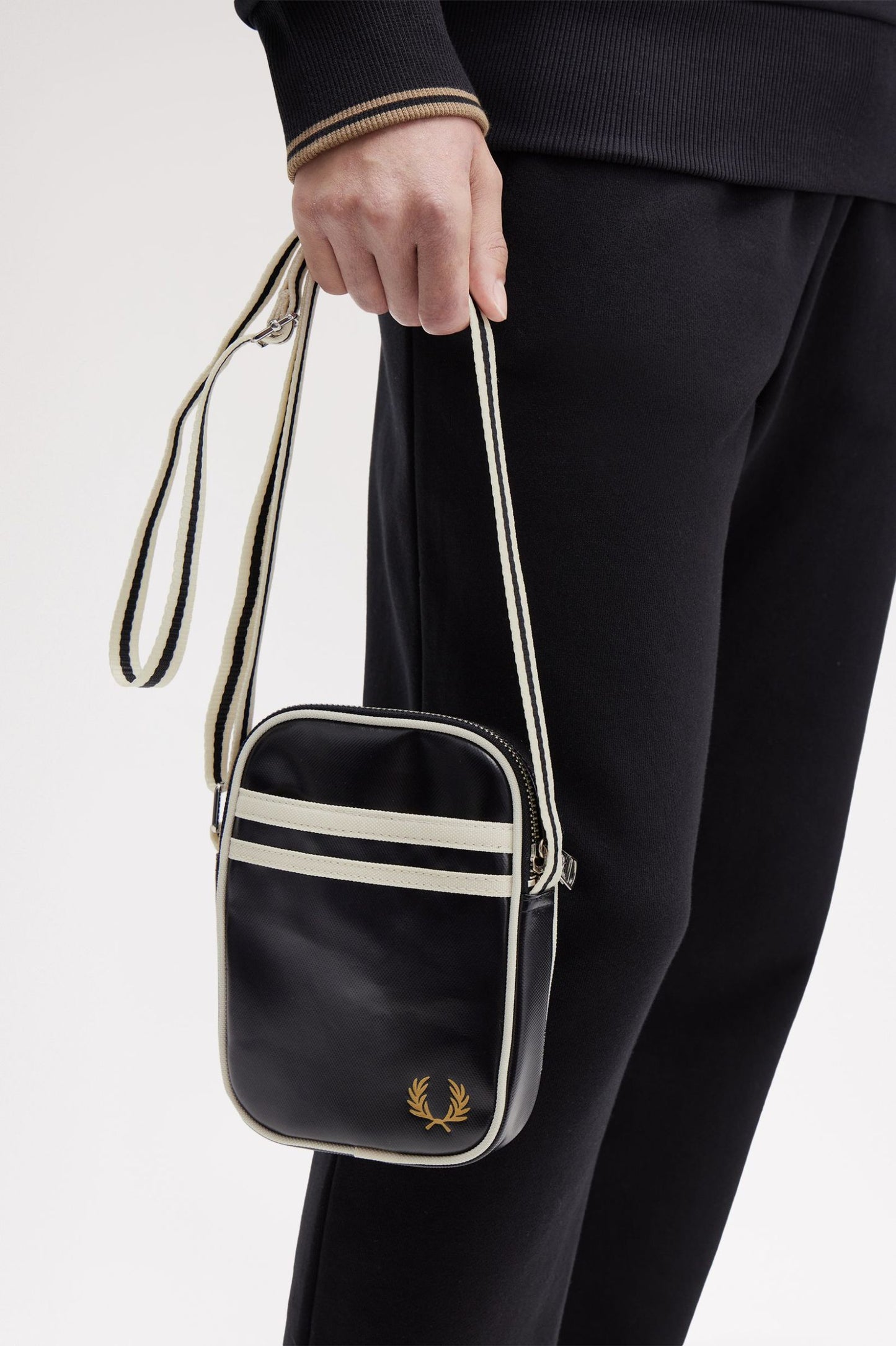 Person holding a black crossbody bag with a brand logo, wearing black pants and a dark sweater.