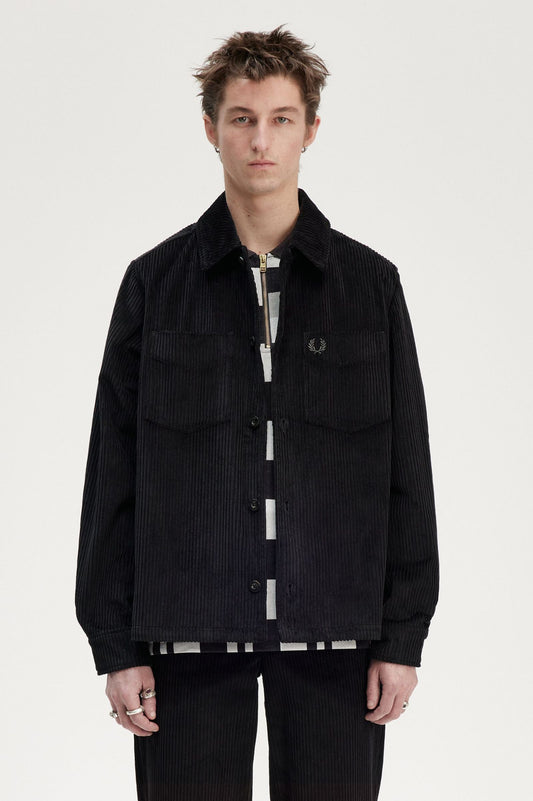 A male model wearing a black Fred Perry Corduroy Overshirt with a collared neckline and long sleeves.