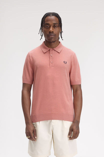 A person wearing a short-sleeved Fred Perry polo shirt in pink, with the brand's logo on the chest.