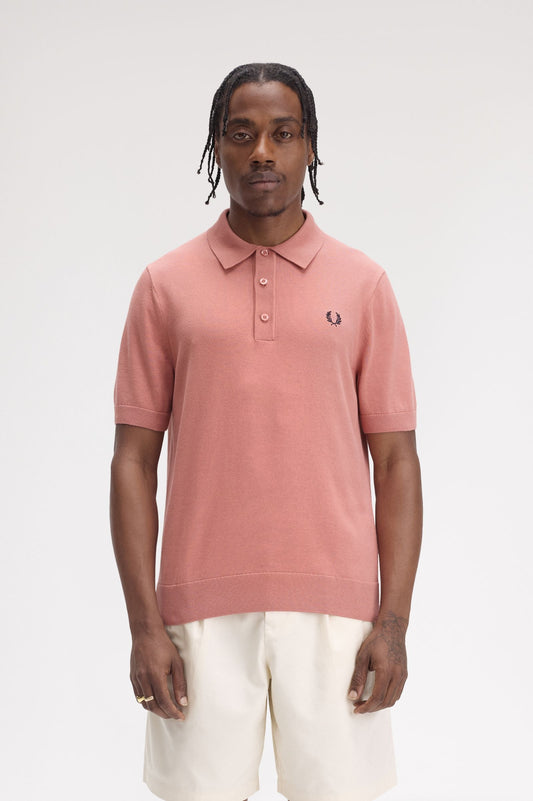 A person wearing a short-sleeved Fred Perry polo shirt in pink, with the brand's logo on the chest.