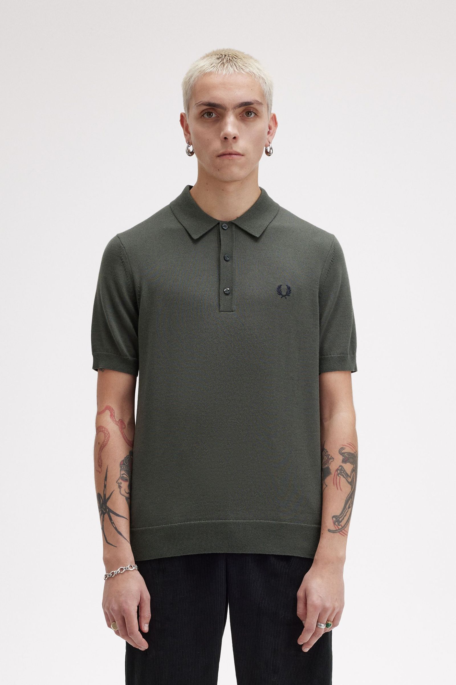 A male model wearing a green Fred Perry fine knit shirt with a collar, button-up neck, and short sleeves.