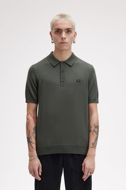 A male model wearing a green Fred Perry fine knit shirt with a collar, button-up neck, and short sleeves.