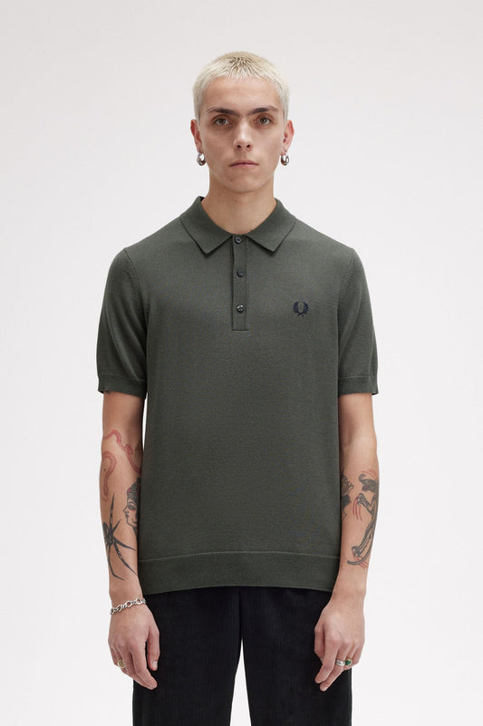 A male model wearing a green Fred Perry fine knit shirt with a collar, button-up neck, and short sleeves.