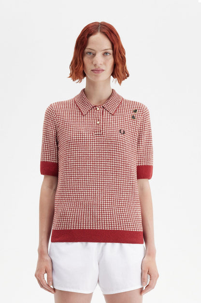 A woman wearing a red and white gingham knitted Fred Perry shirt with short sleeves, collar, and button-up front, paired with white shorts.