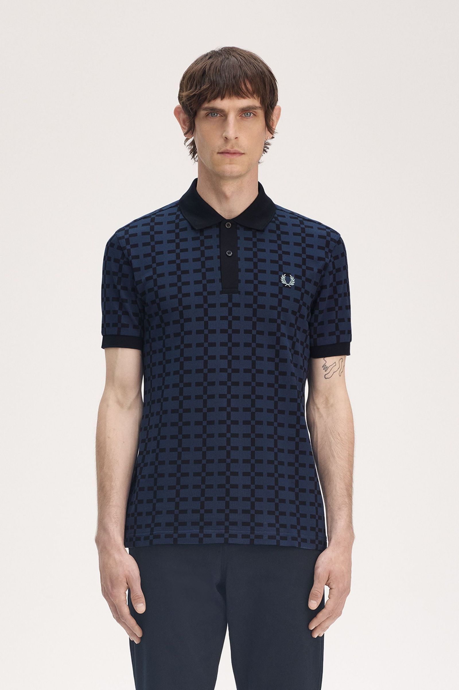 A man wearing a navy blue geometric patterned Fred Perry polo shirt with the brand's logo on the chest.