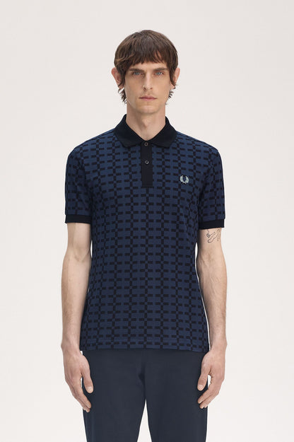 A man wearing a navy blue geometric patterned Fred Perry polo shirt with the brand's logo on the chest.