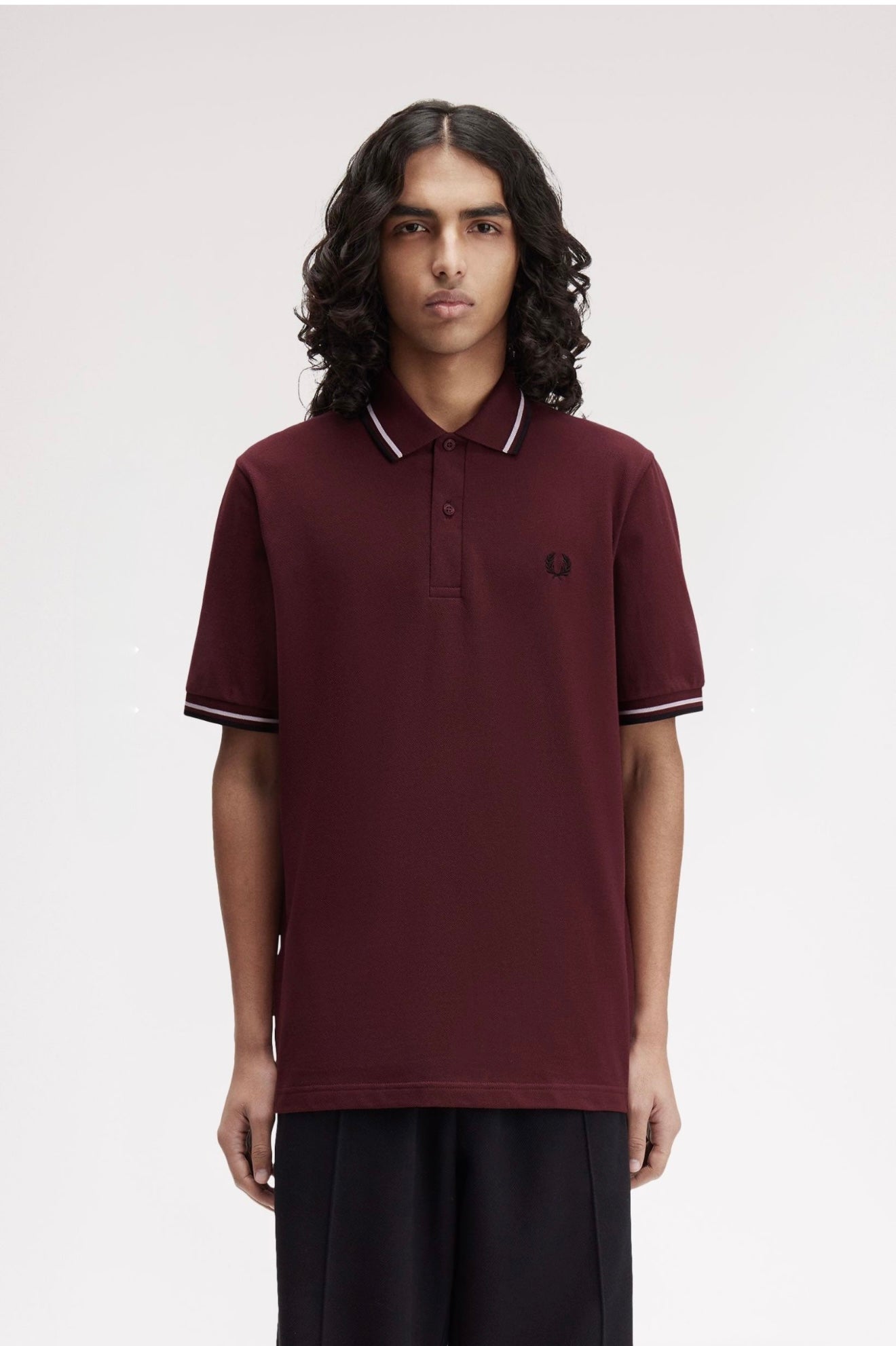 Person wearing a maroon polo shirt with a brand logo on a plain background