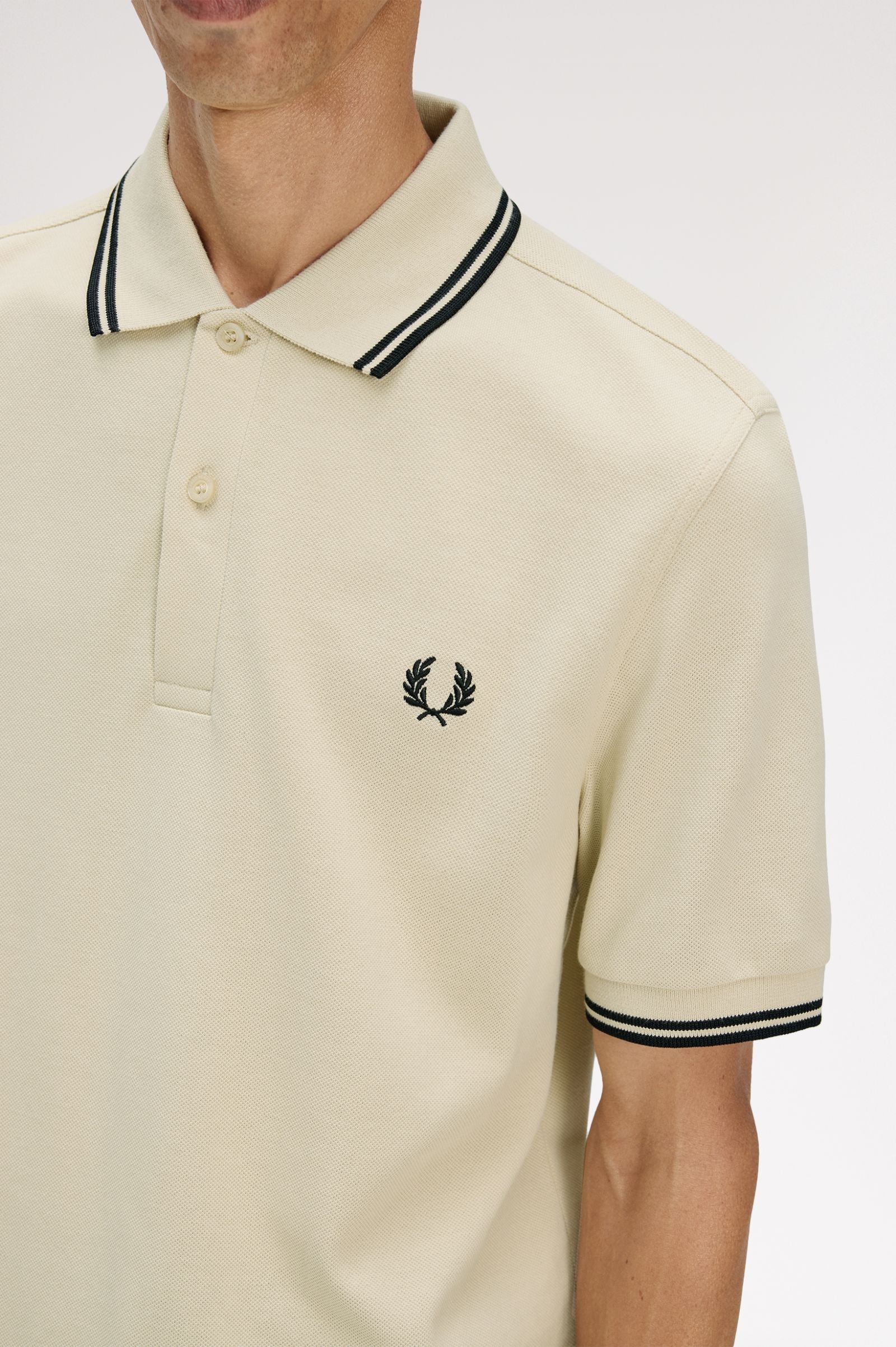 Beige polo shirt with black and white trim worn by a person on a light gray background