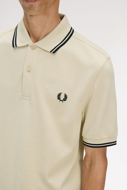 Beige polo shirt with black and white trim worn by a person on a light gray background