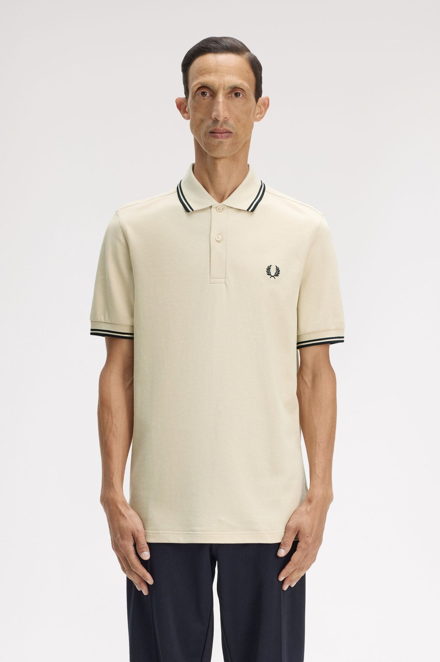 Man wearing a cream polo shirt with black trim and a visible brand logo on a white background
