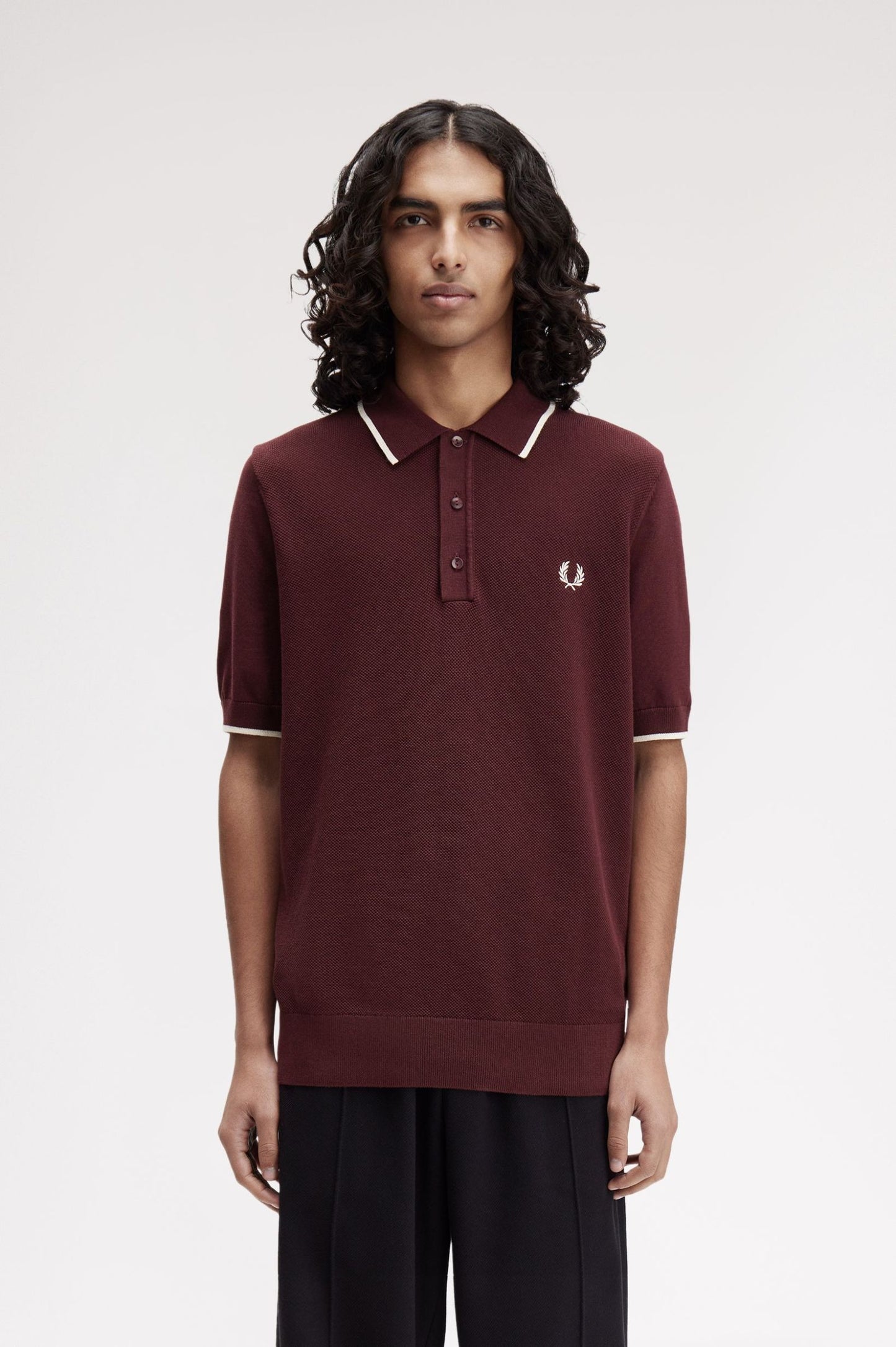 Person wearing a maroon polo shirt with white trim on a plain background