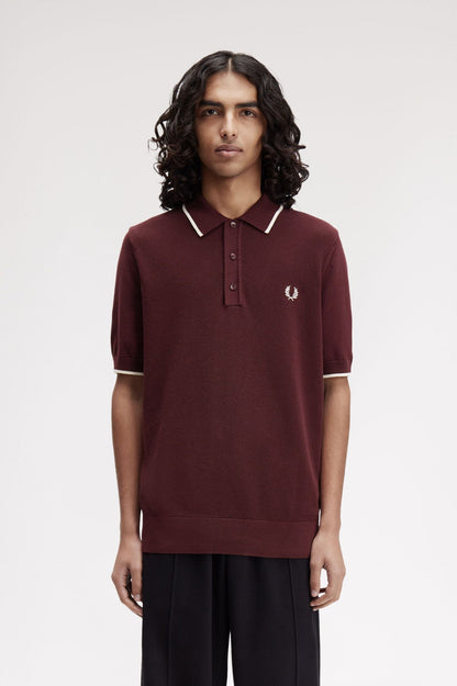 Person wearing a maroon polo shirt with white trim on a plain background