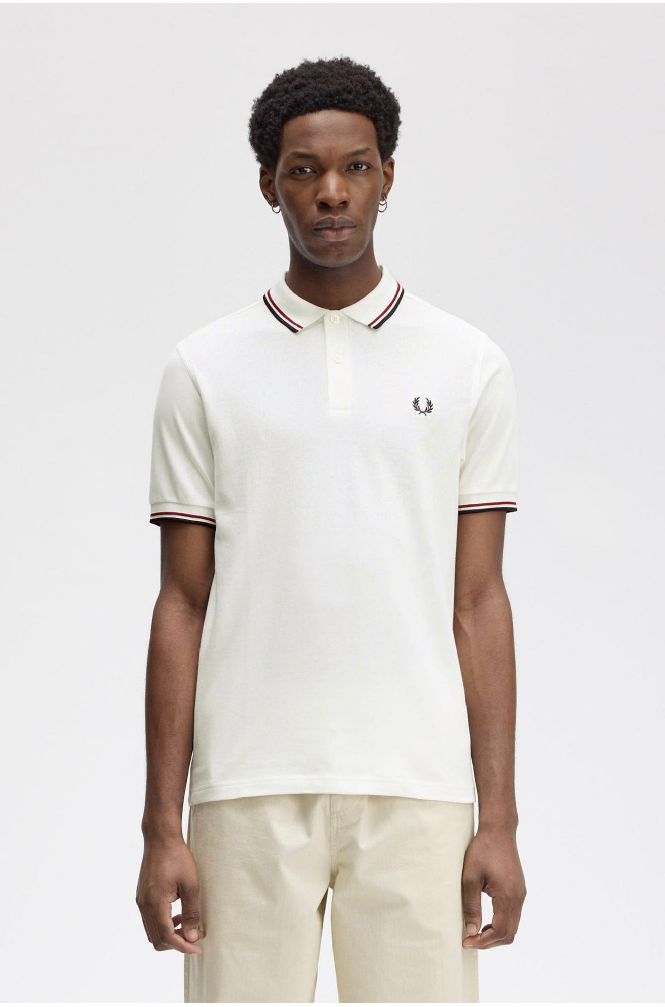 Person wearing a white polo shirt with a brand logo on a plain background