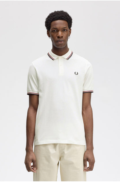 Person wearing a white polo shirt with a brand logo on a plain background