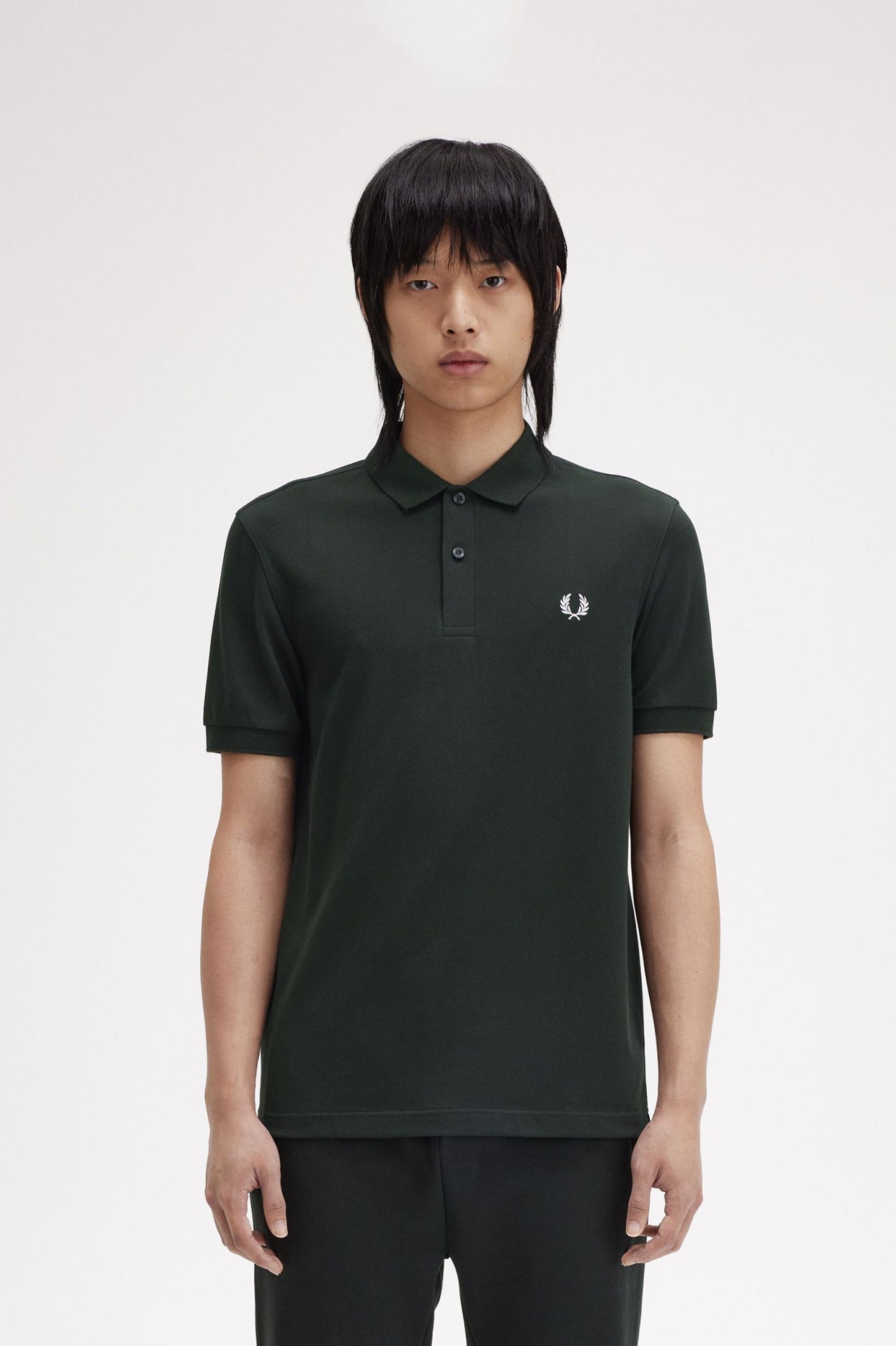 A person wearing a green Fred Perry polo shirt with a collar and two-button placket.