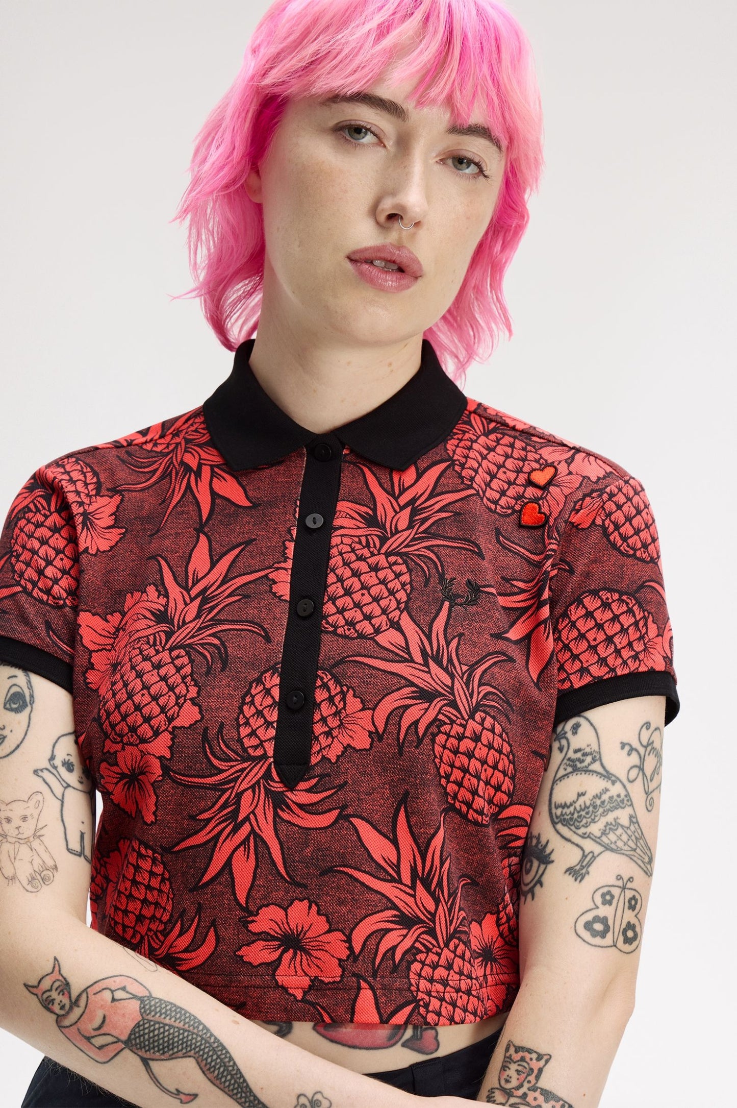 Person wearing a red and black patterned shirt with pink hair on a white background