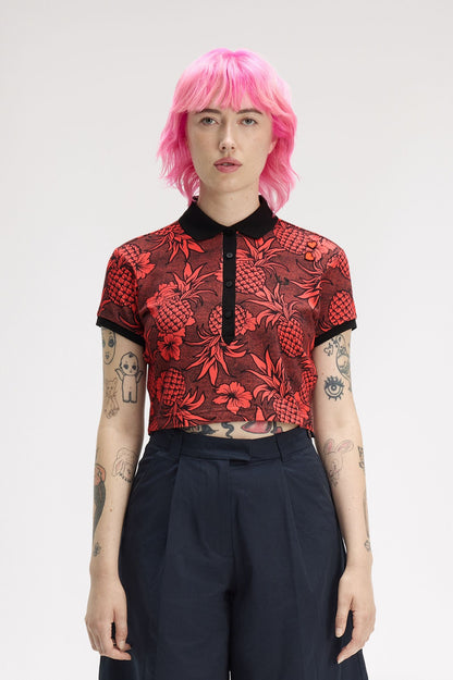 Person wearing a red patterned top and black pants with pink hair on a white background