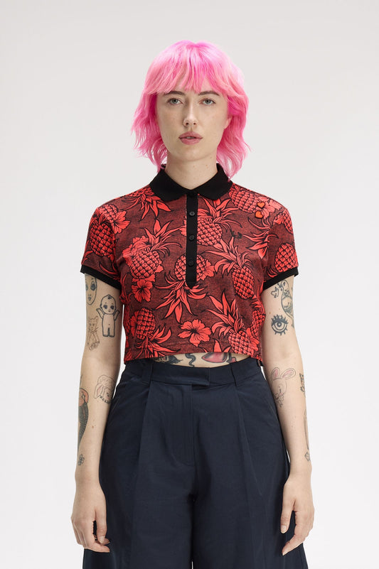 Person wearing a red patterned top and black pants with pink hair on a white background