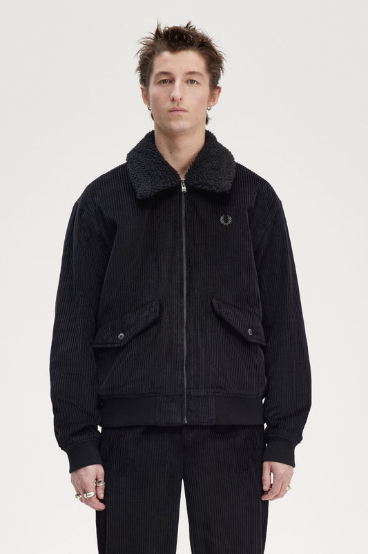 A male model wearing a black cord bomber jacket with a removable collar, featuring a round neckline and long sleeves.